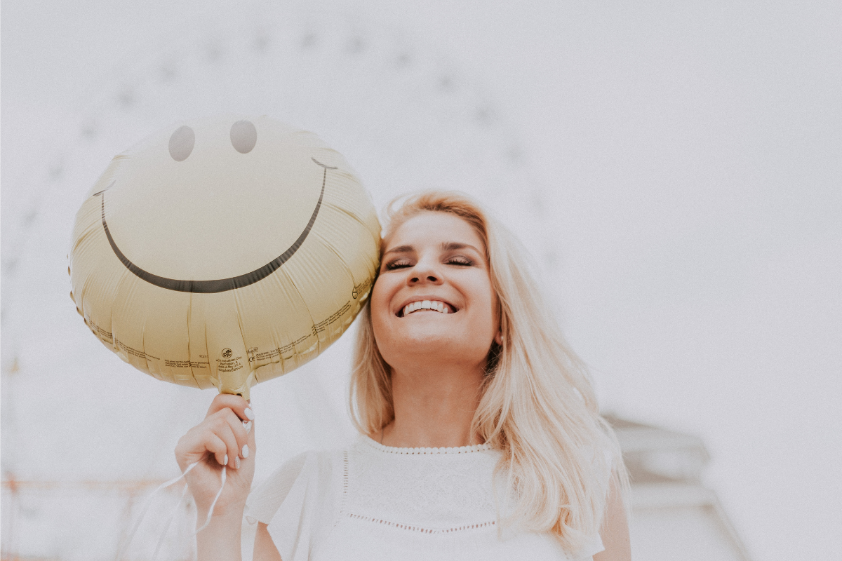 An image of a happy woman holding a smiley balloon.
