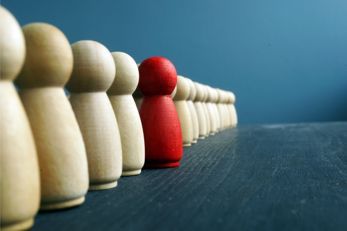 A line of chess pieces with one red pawn standing out.