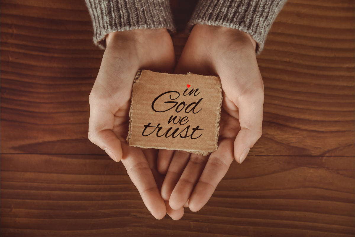 A pair of hands holding a cardboard cut out with the words 'In God We Trust.'