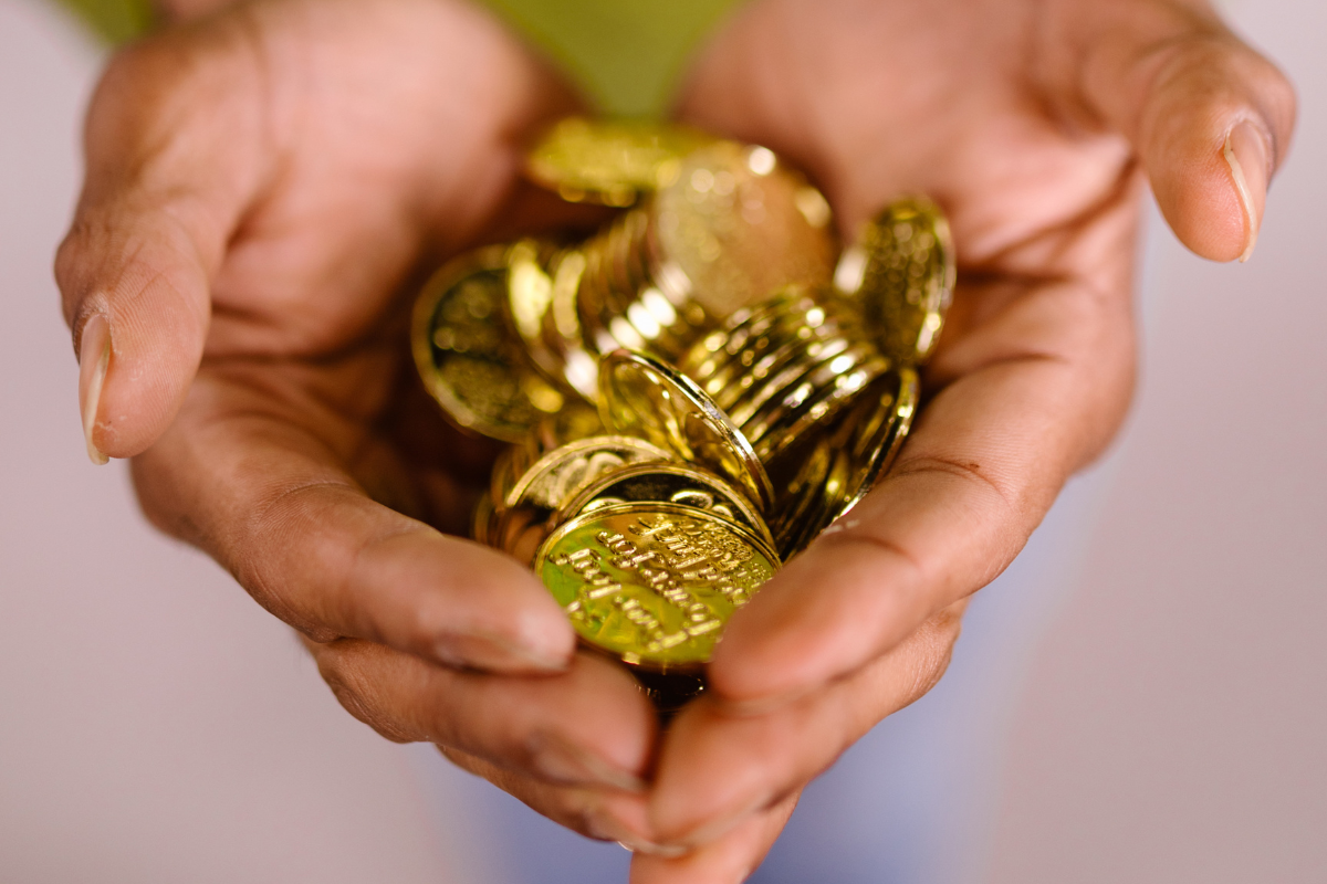 An image of hands holding a lot of gold coins.