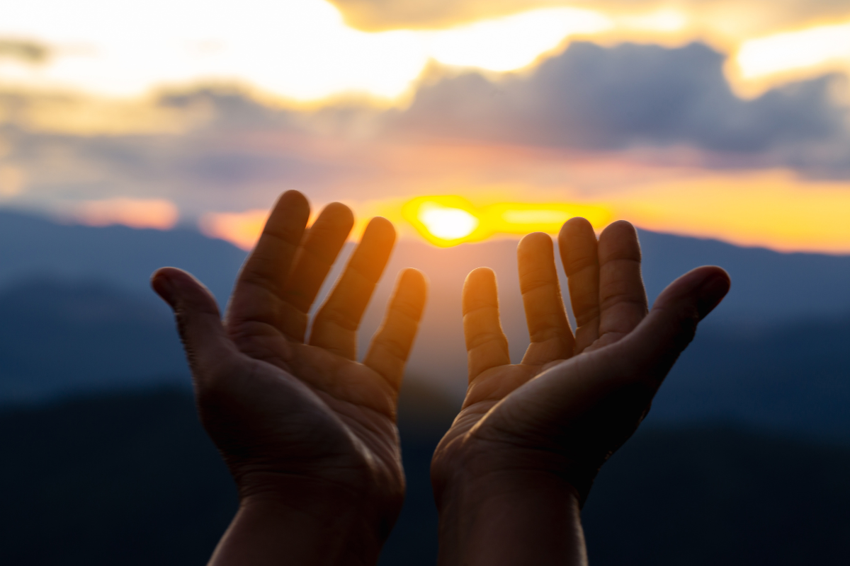 An image of open hands, facing a sunset view.
