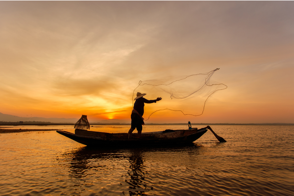 A fisherman on his boat during sunset.