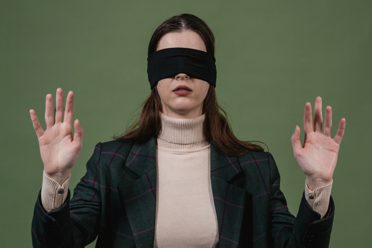 A woman blindfolded with hands raised.