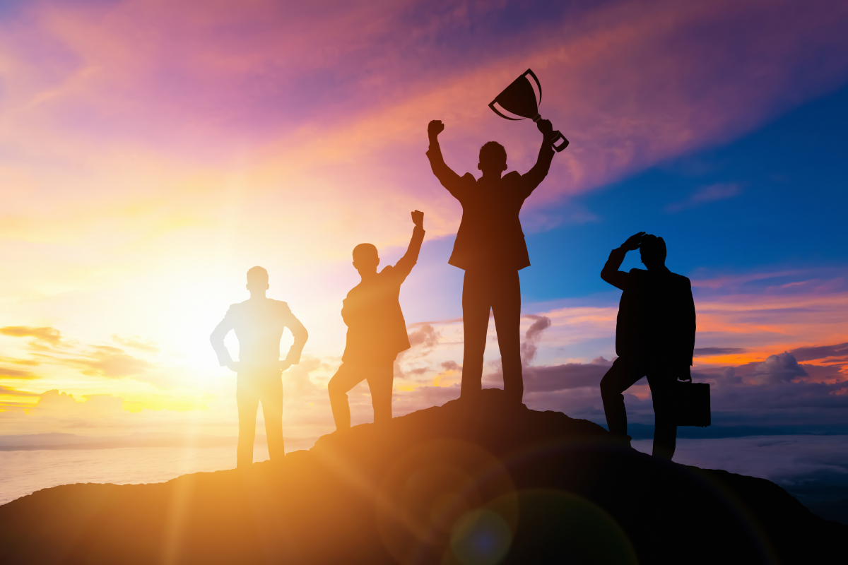 A group of businessmen on top of a mountain, with one being triumphant.