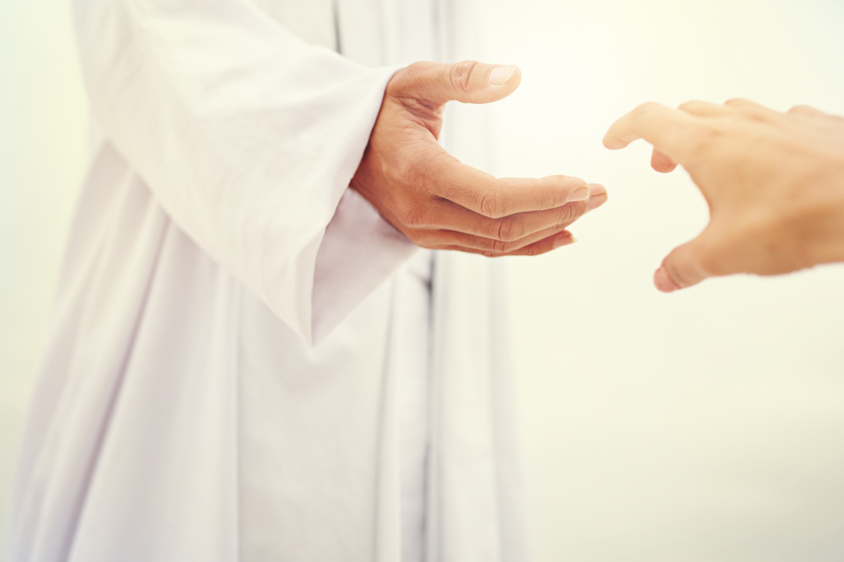 A person in a white robe reaching out for another person's hand.