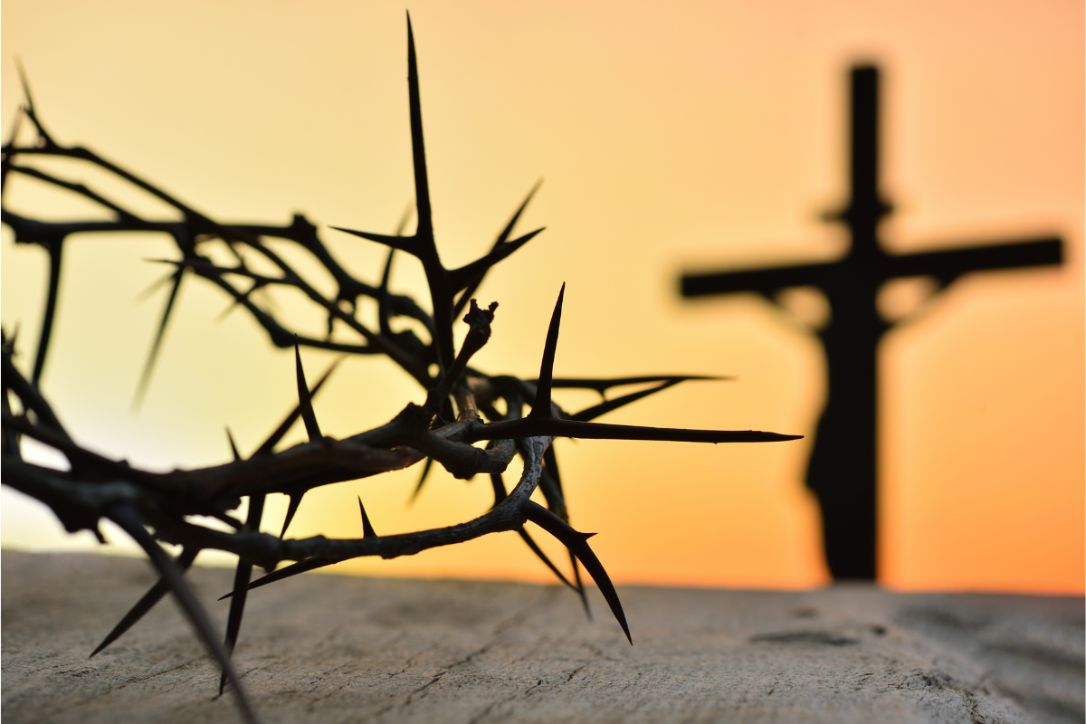 A crown of thorns in front of Jesus' silhouette on the cross.