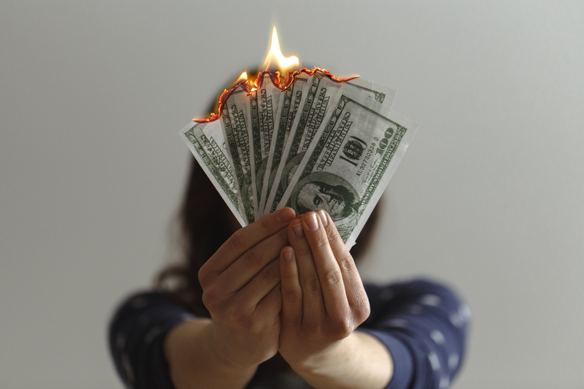 An image of a person holding hundred dollar bills in flames.