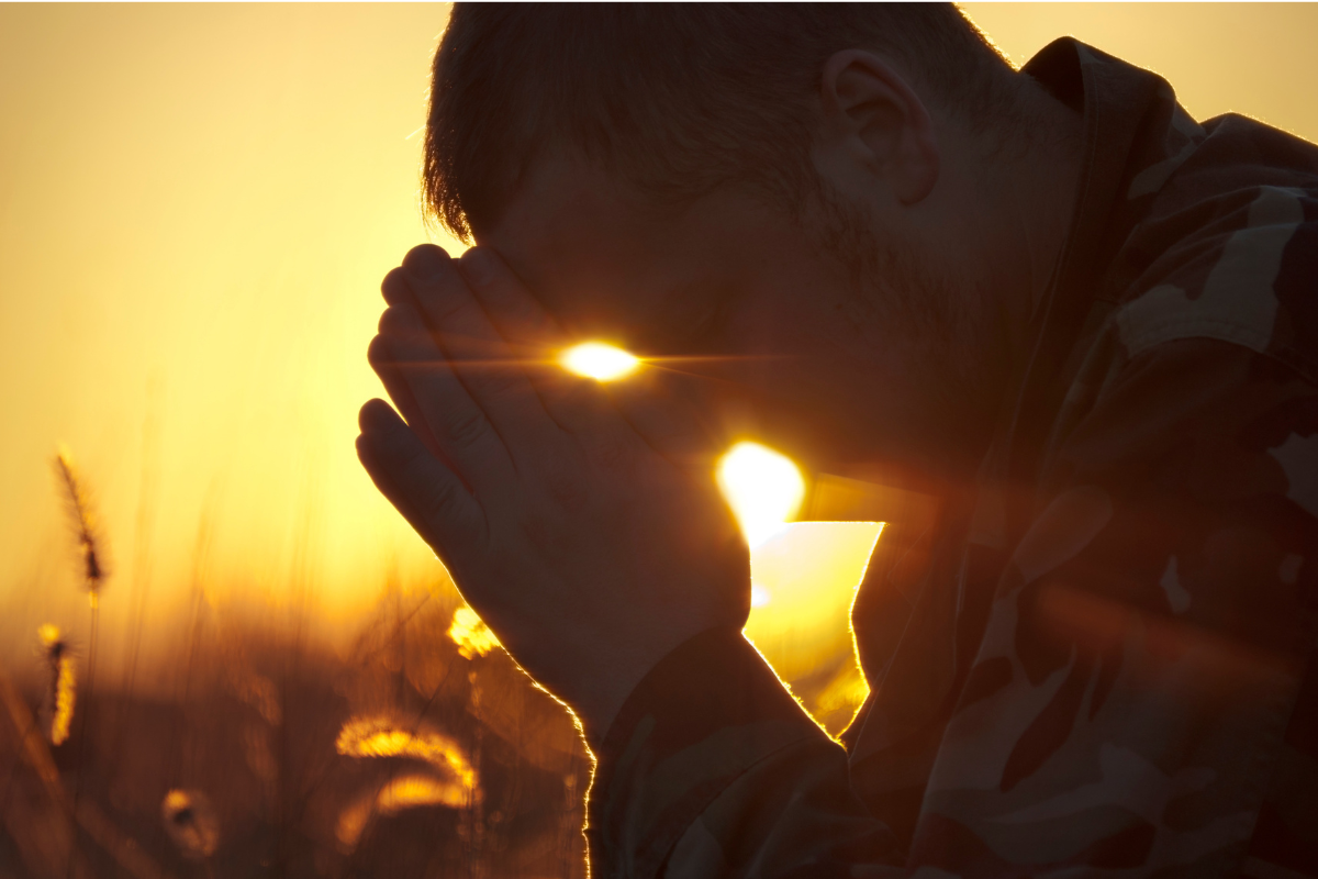 A silhouette of a man in prayer during sunrise or sunset.