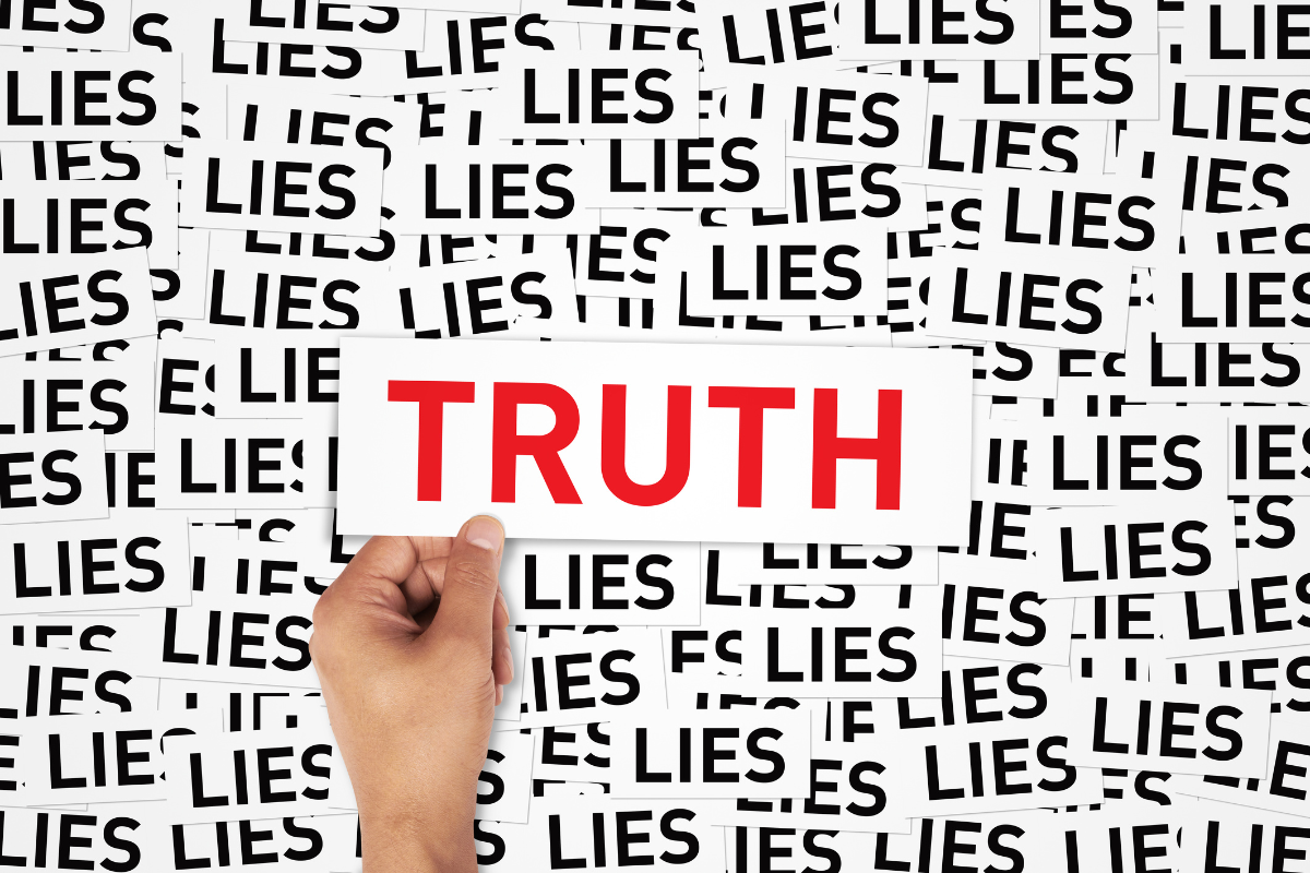 A person holding a piece of paper with the word TRUTH amidst papers with the word LIES.
