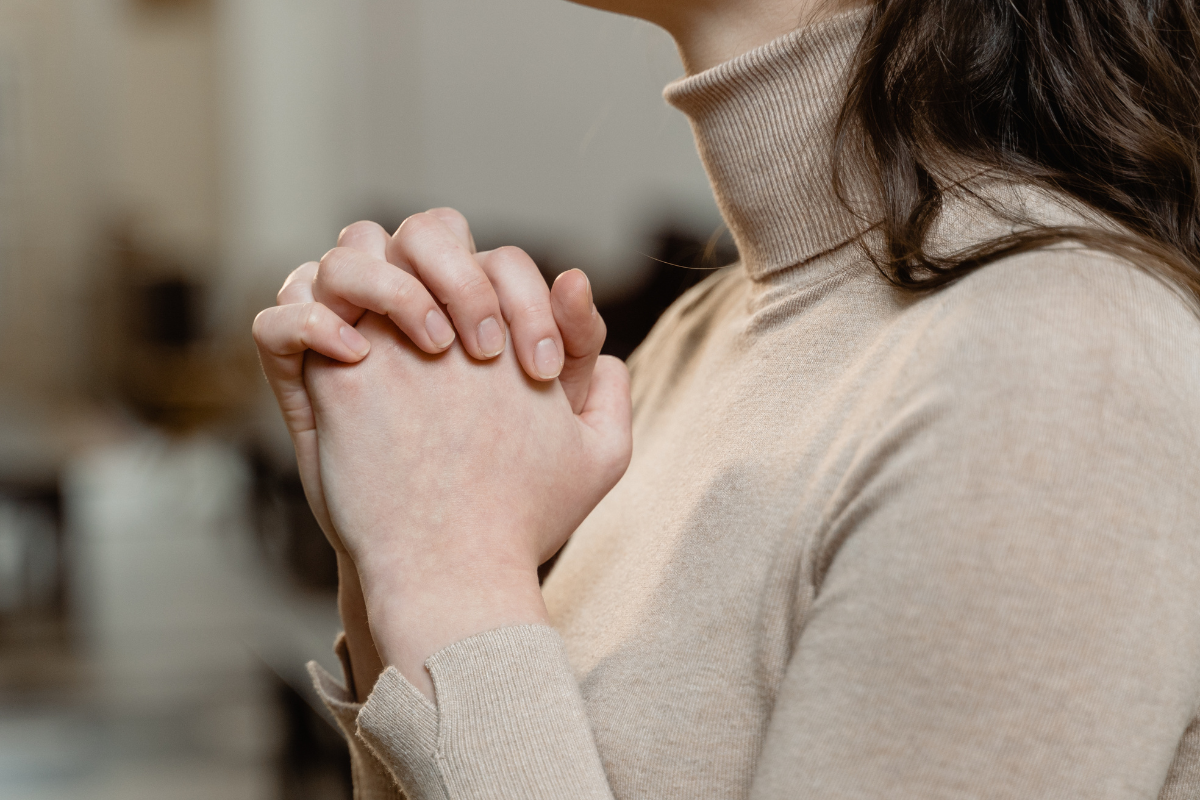 A woman with her hands clasped together, signifying believing.