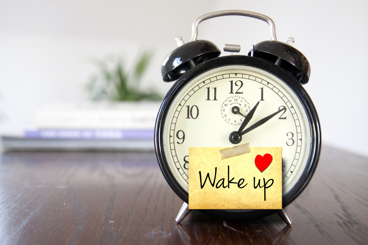 An alarm with a sticky note, with the words WAKE UP and a small red heart on it.