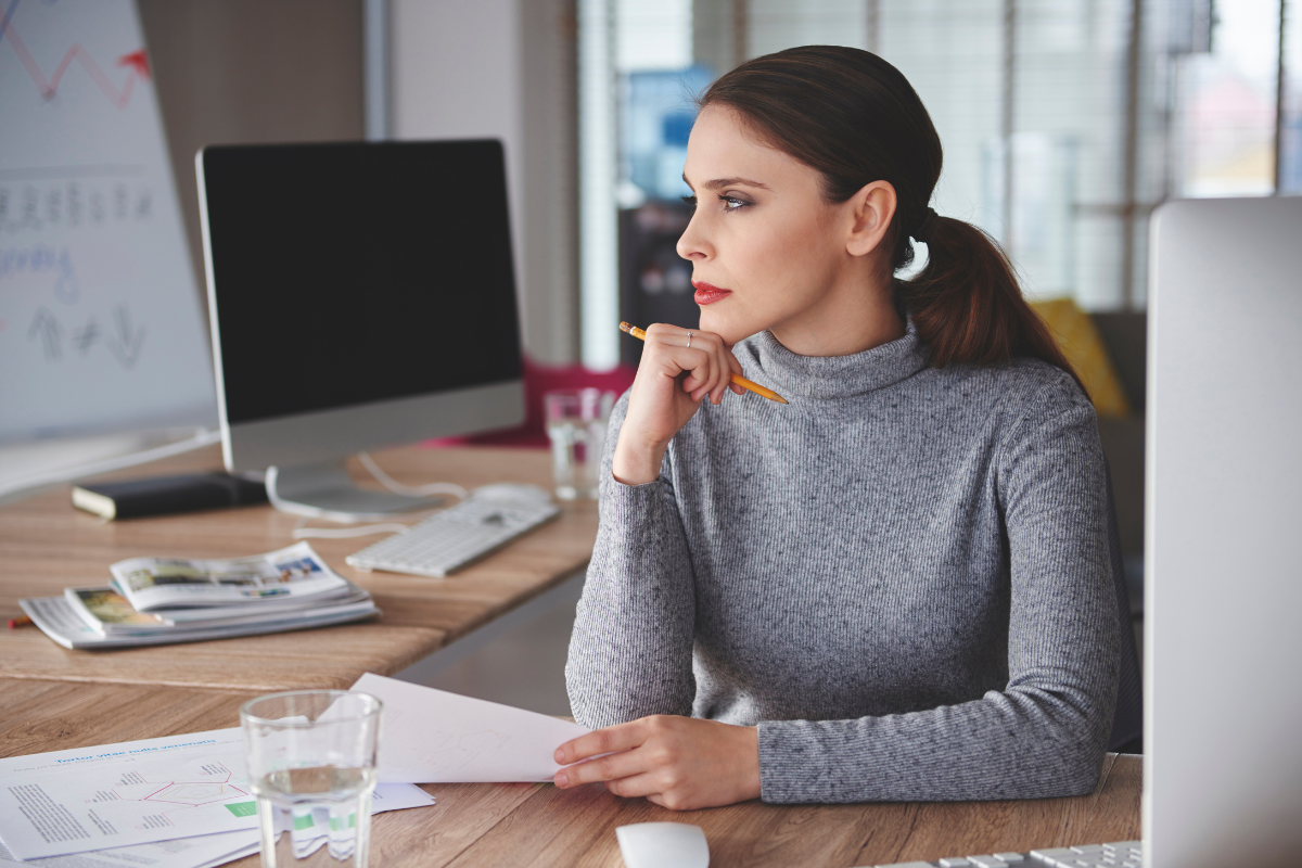 A woman in an office, thinking afar.