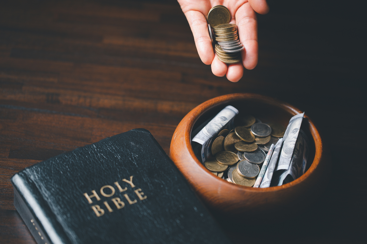 Tithes and offerings being placed inside a wooden bowl beside a Bible.