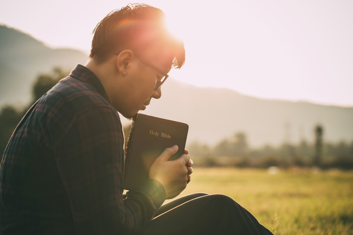 A man holding a Bible with a beautiful landscape in the background.
