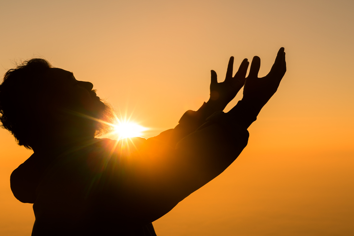 A silhouette of a man, holding his arms and hands high up.
