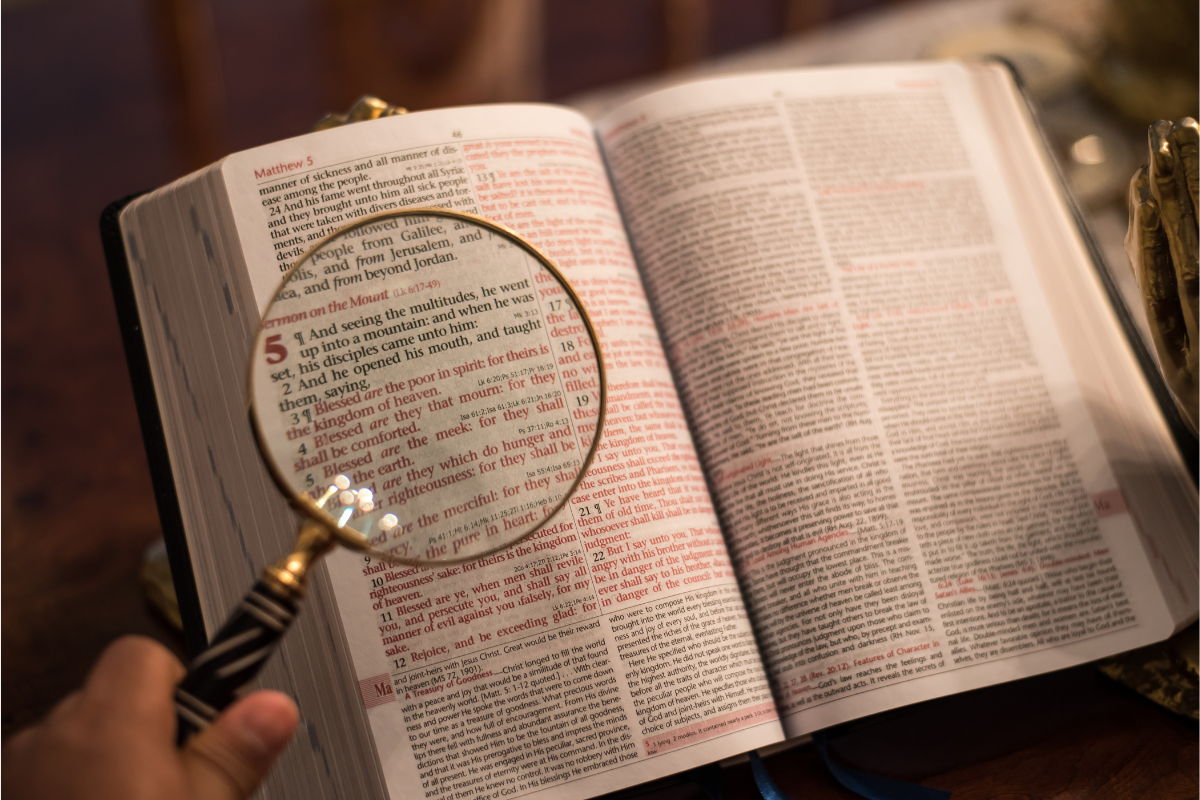 A magnifying glass being hovered over a part of the Bible.