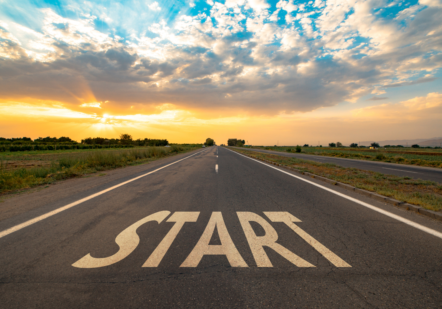 A long highway going towards a sunset, with the word START written on the road.