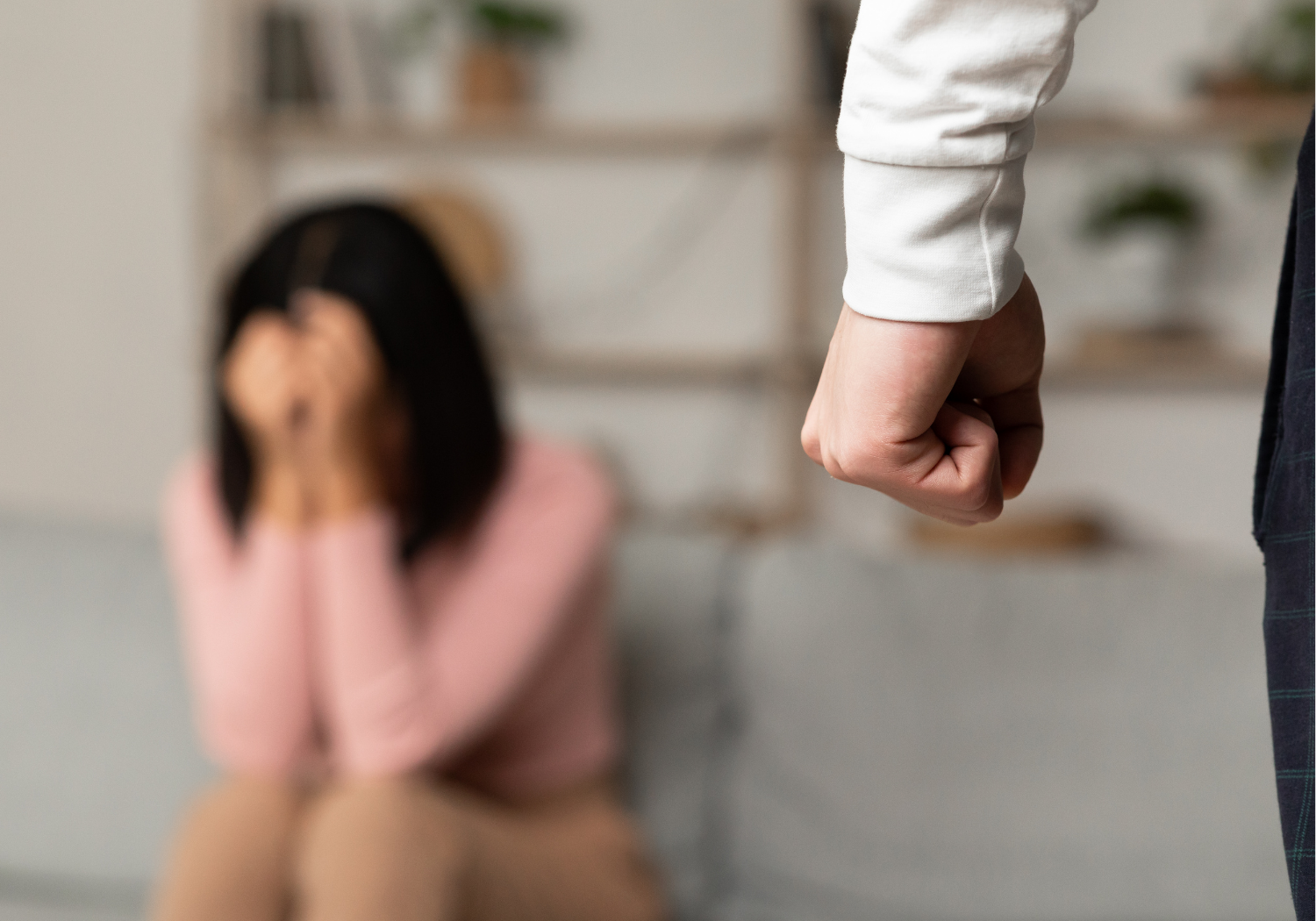 A man with a closed fist and a woman in the background, illustrating domestic violence.