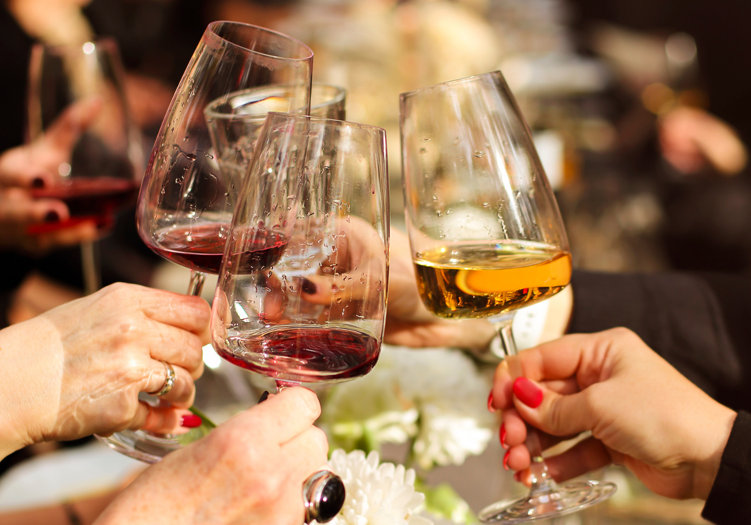 Hands holding wine glasses with wine.