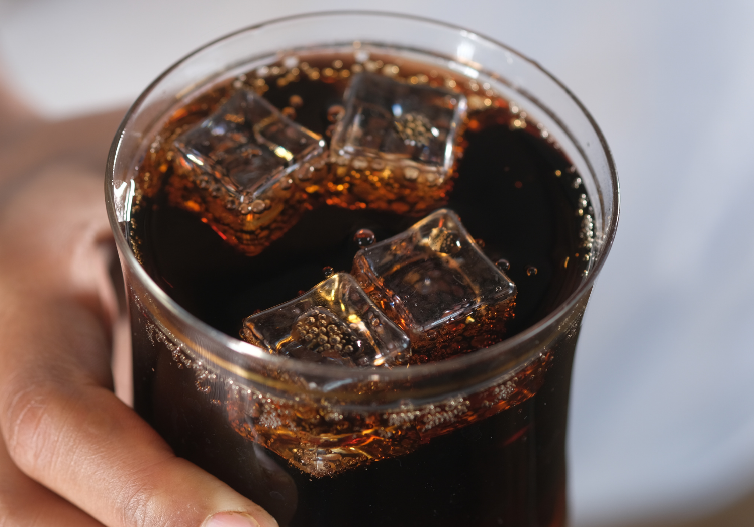 A person holding a glass of carbonated beverage.