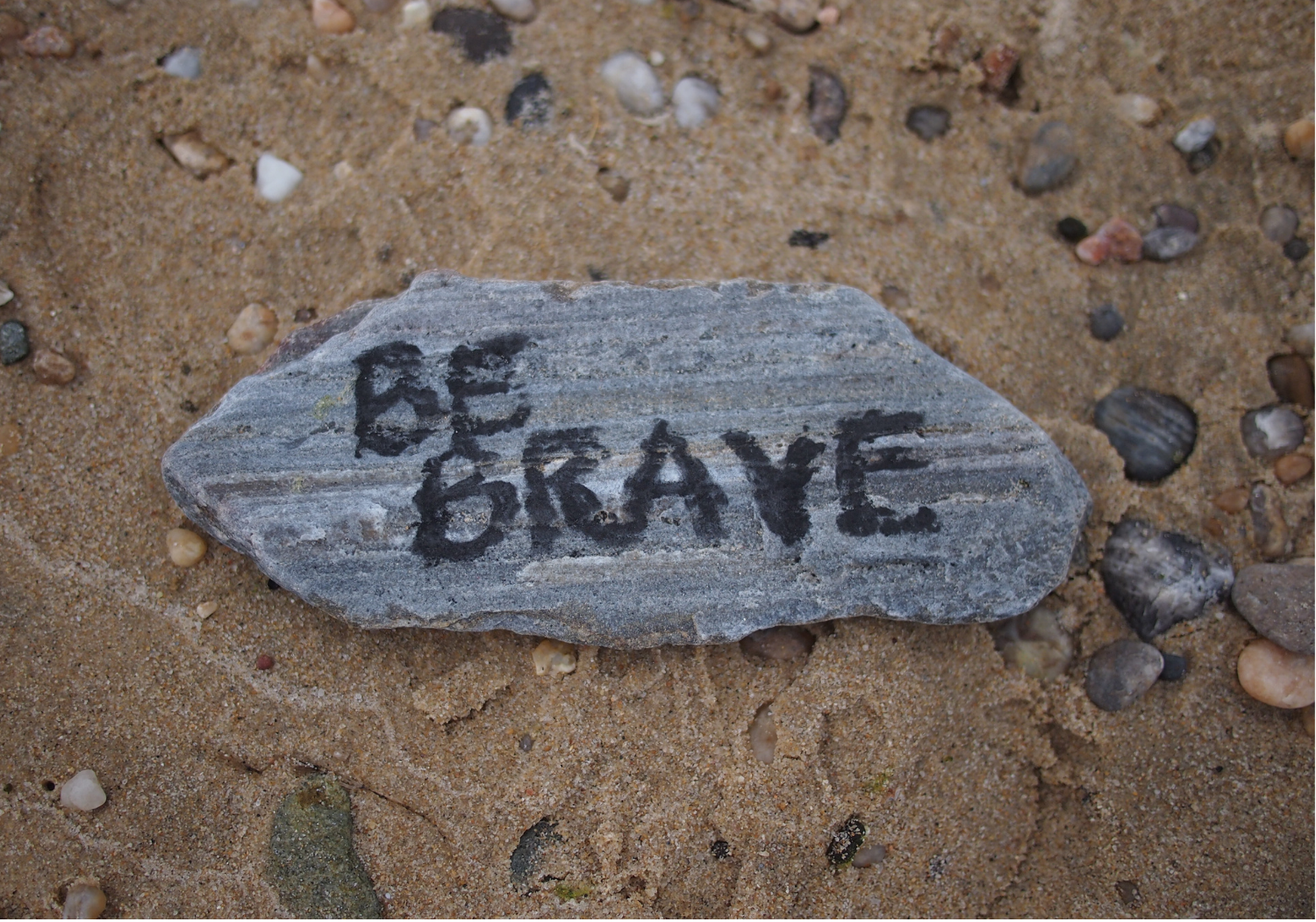 The words 'Be Brave' written on a sedimentary rock plate.