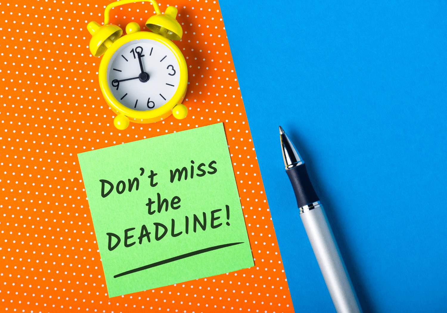 A small yellow clock and a pen, with a sticky note with the words "Don't Miss the Deadline!"