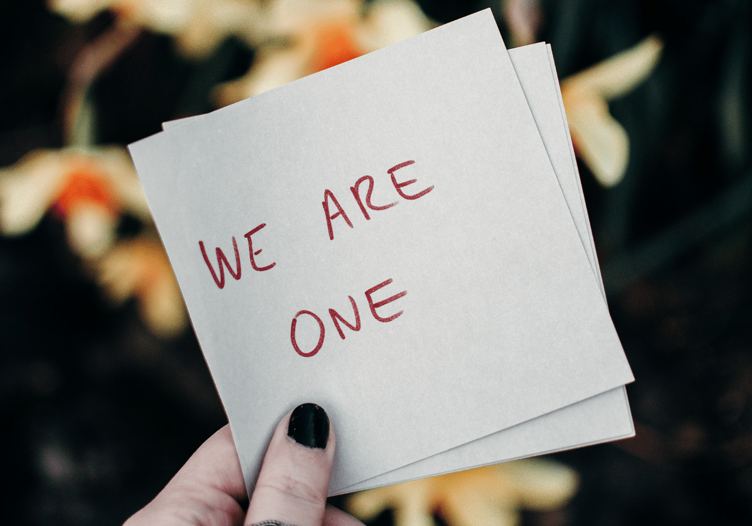 A hand holding a paper with the words WE ARE ONE.